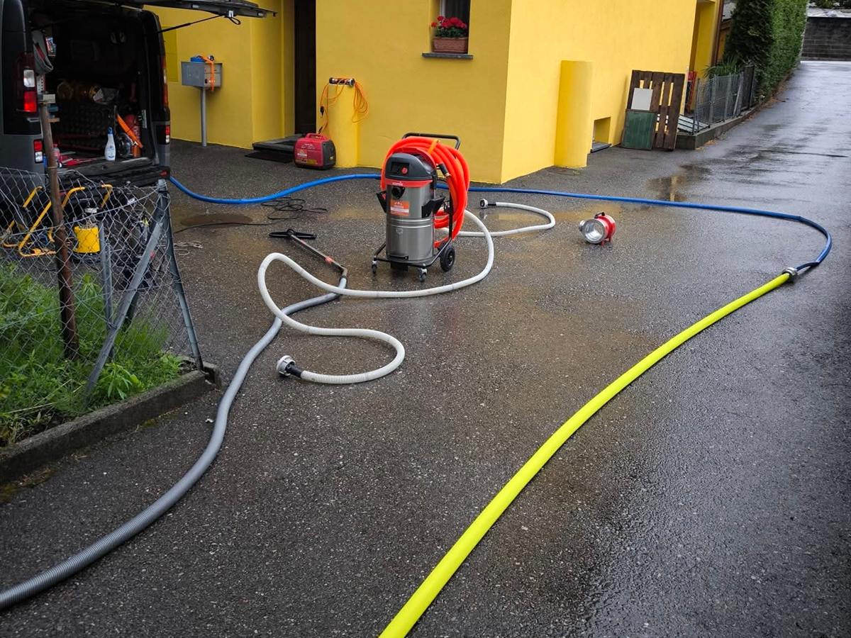 Furgone aperto davanti a una casa, aspiratore e tubi stesi sul piazzale bagnato